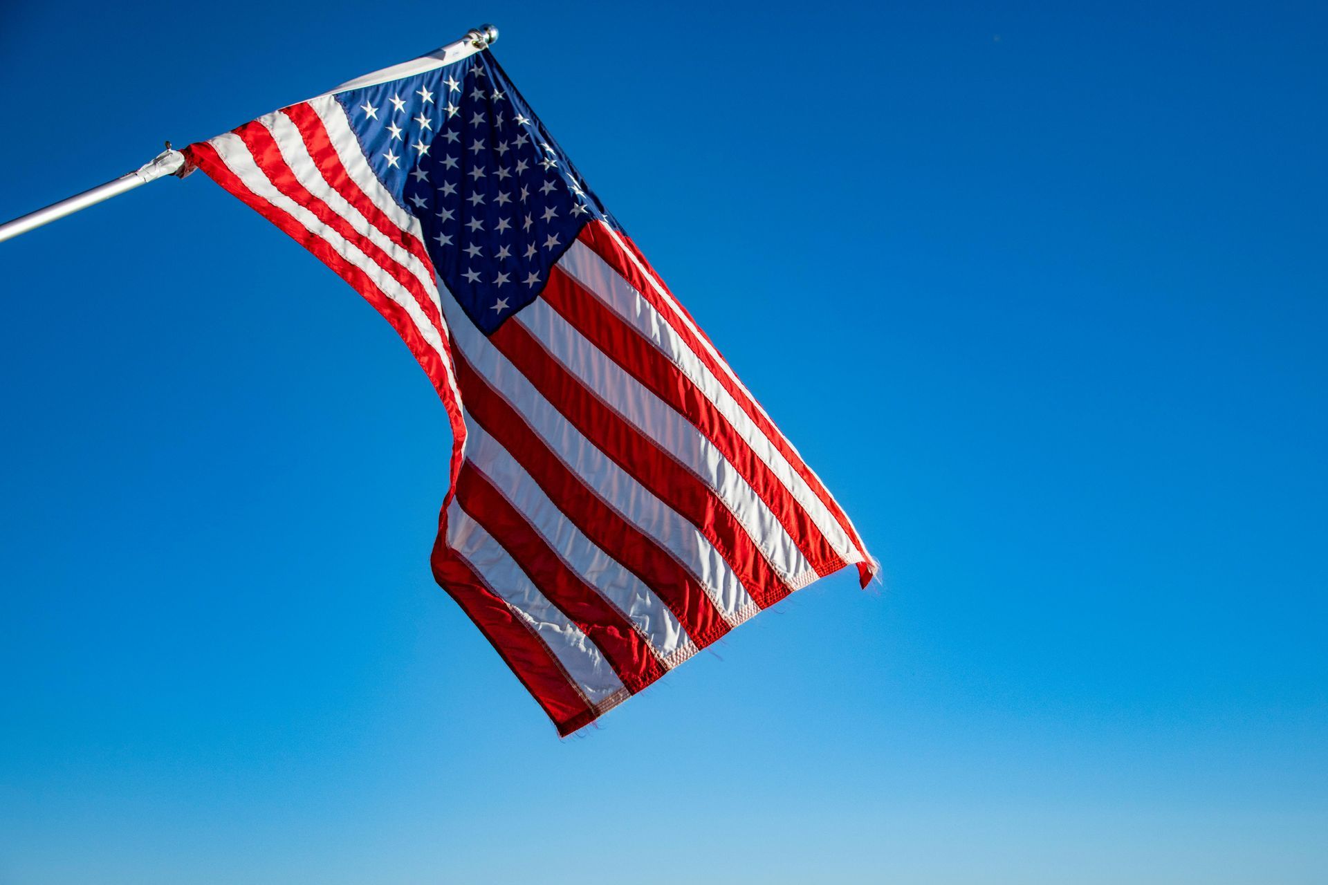 An american flag is flying in the wind against a blue sky.