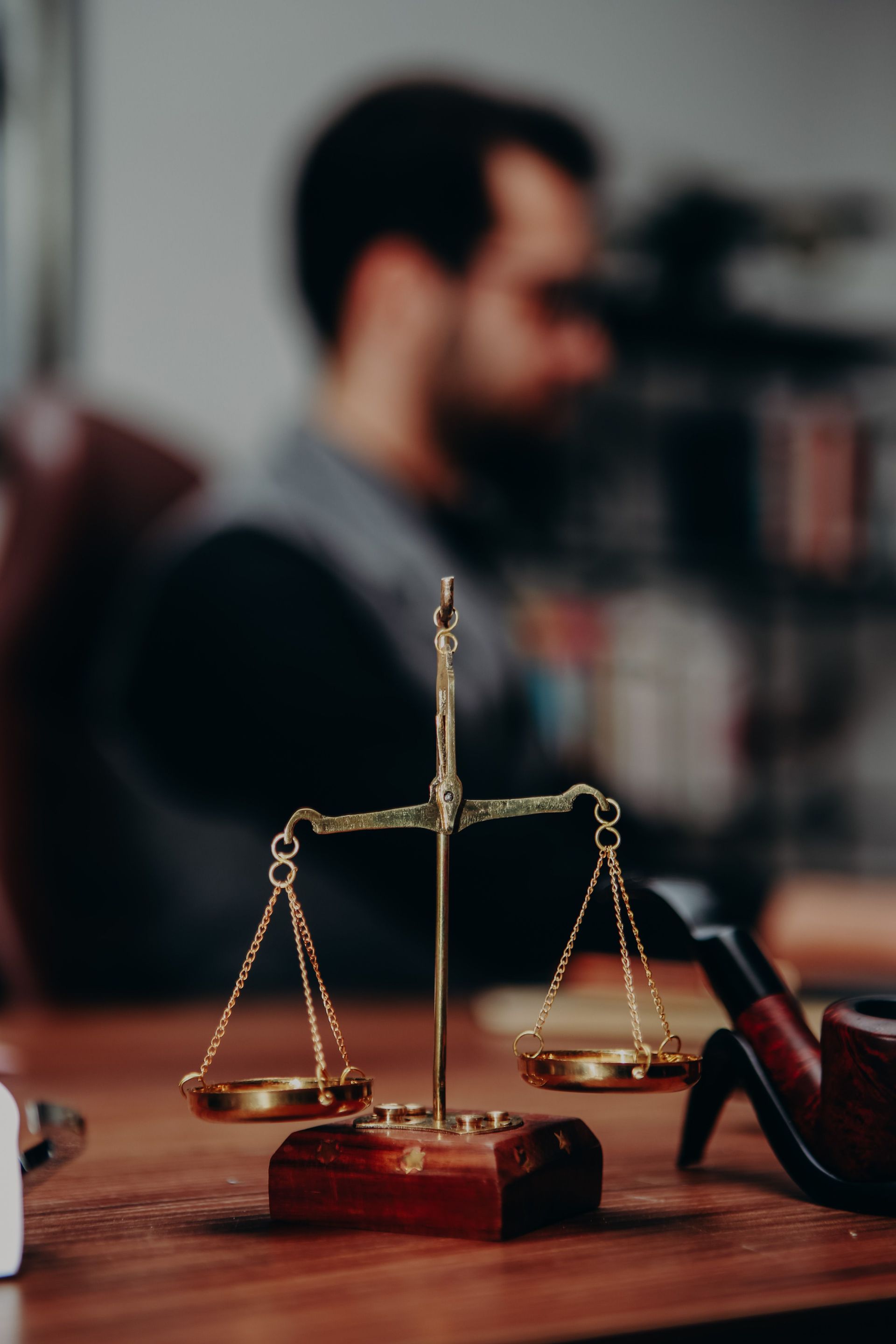 Brass scales of justice on a desk with a blurred lawyer in the background