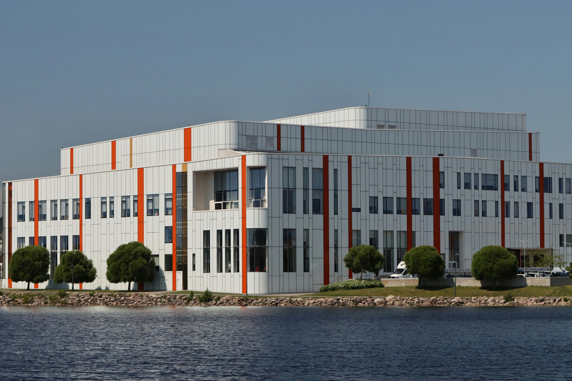 A large white building with red stripes on the side is next to a body of water