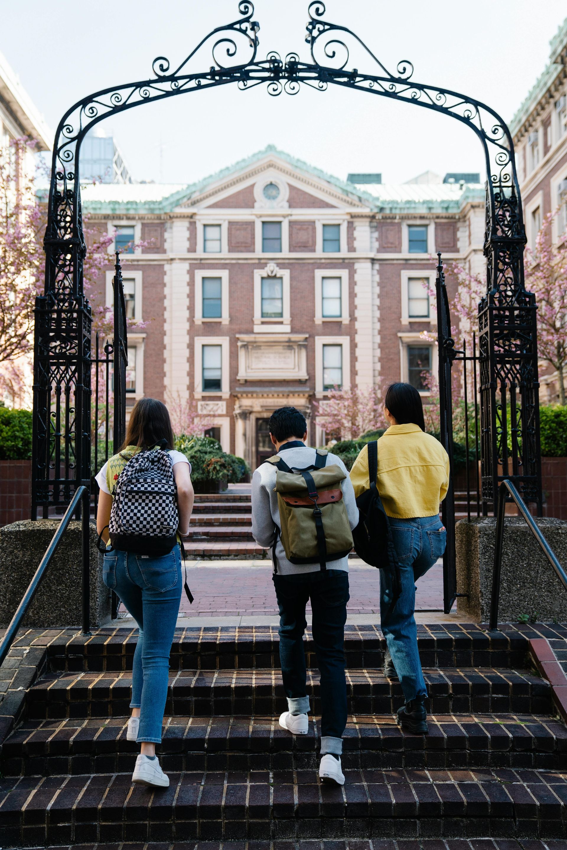 Three people are walking down stairs towards a large building.