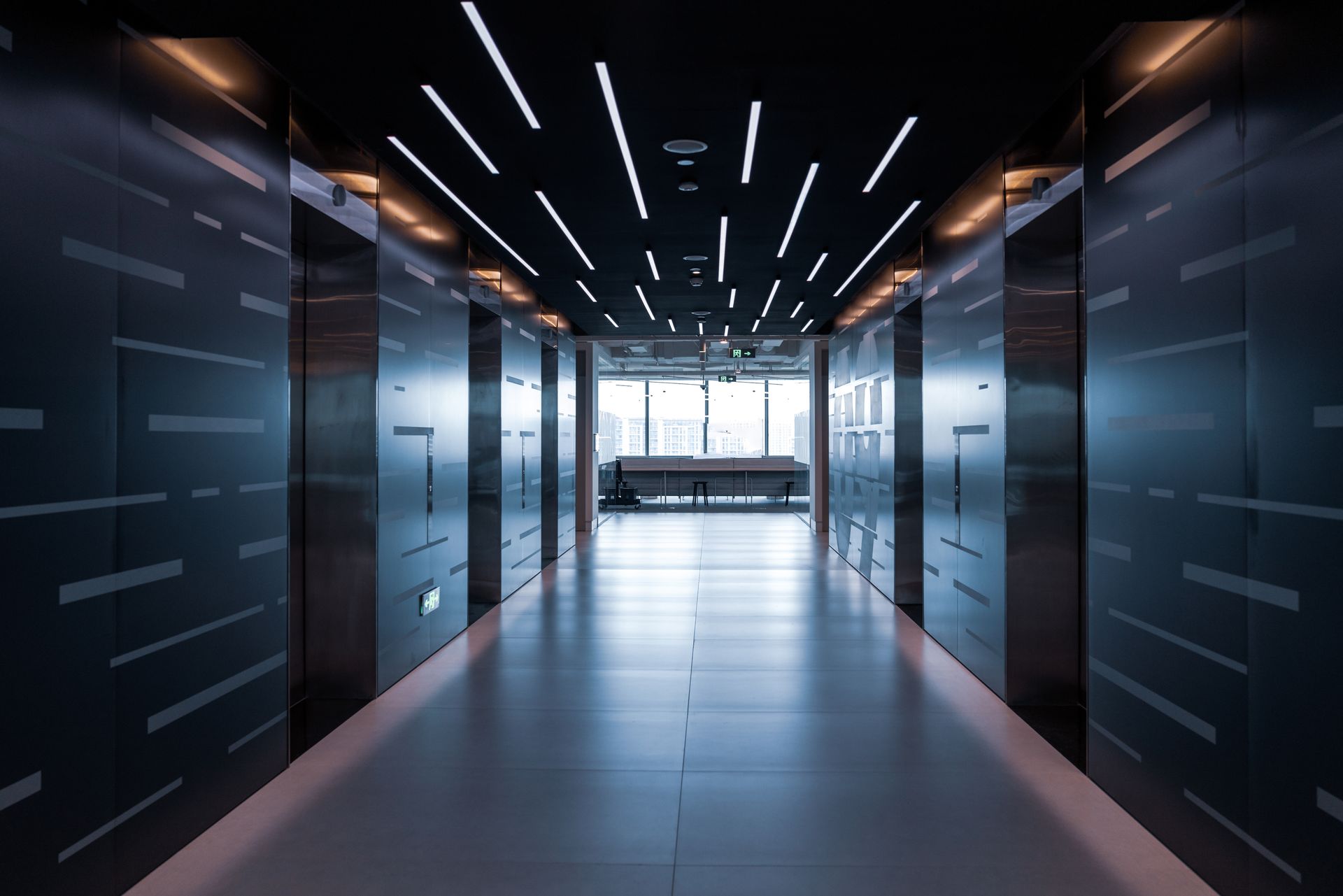 A long hallway with a lot of doors and lights on the ceiling.