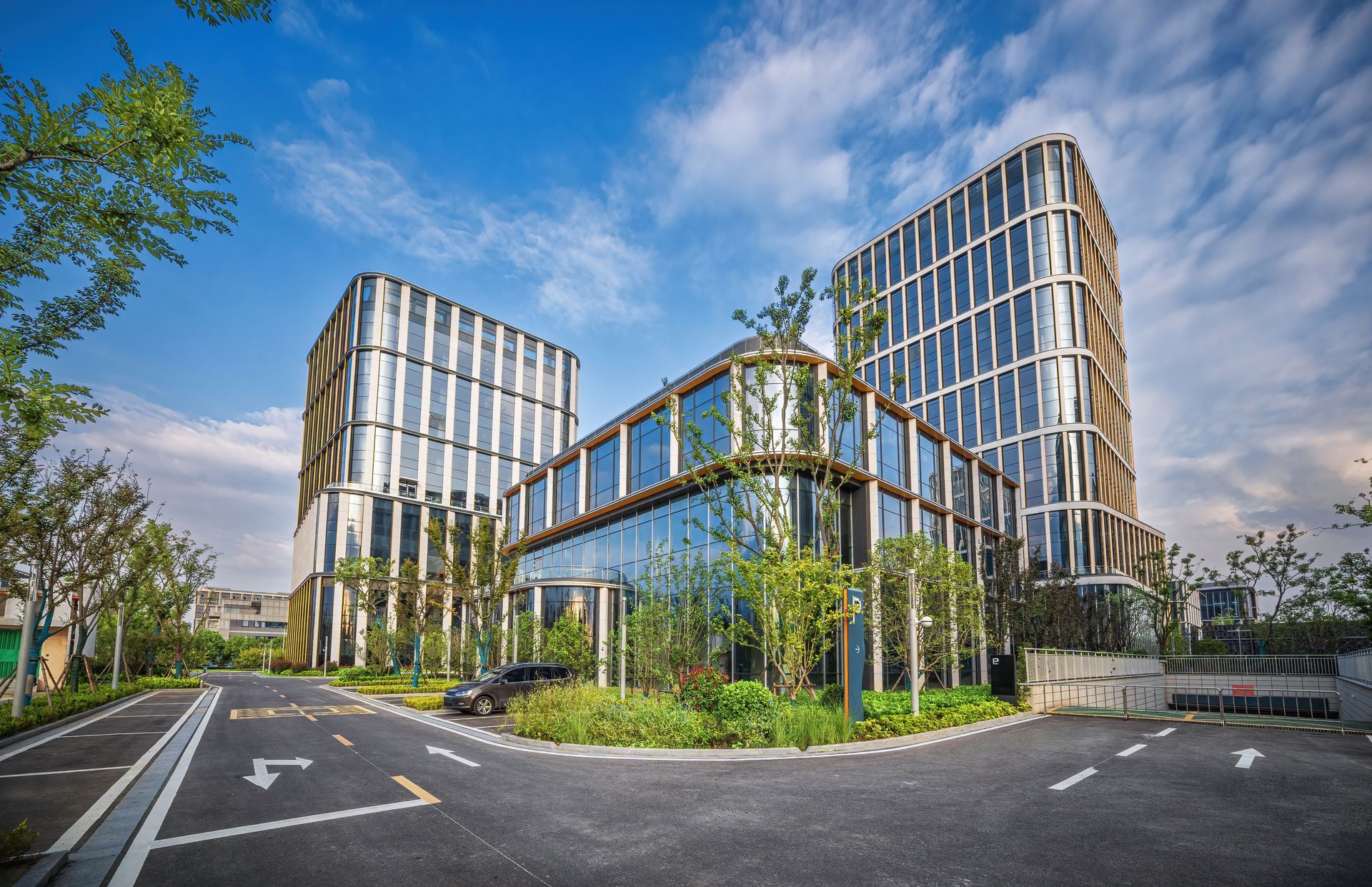 A large building with a lot of windows is surrounded by trees and a parking lot.