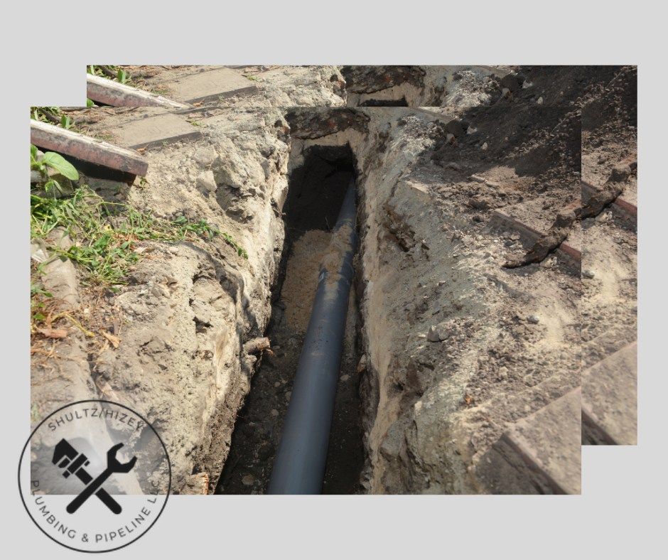 A trench with a gray pipe running through it, likely for plumbing work outdoors.