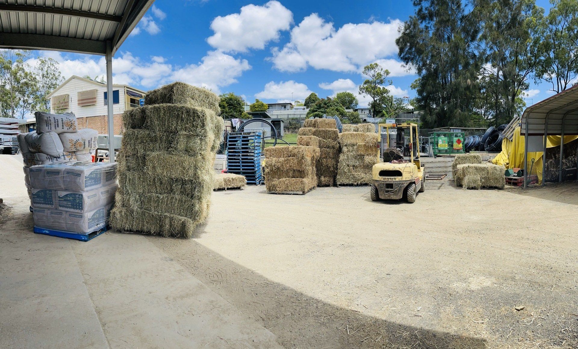 A forklift is moving hay bales in a yard.
