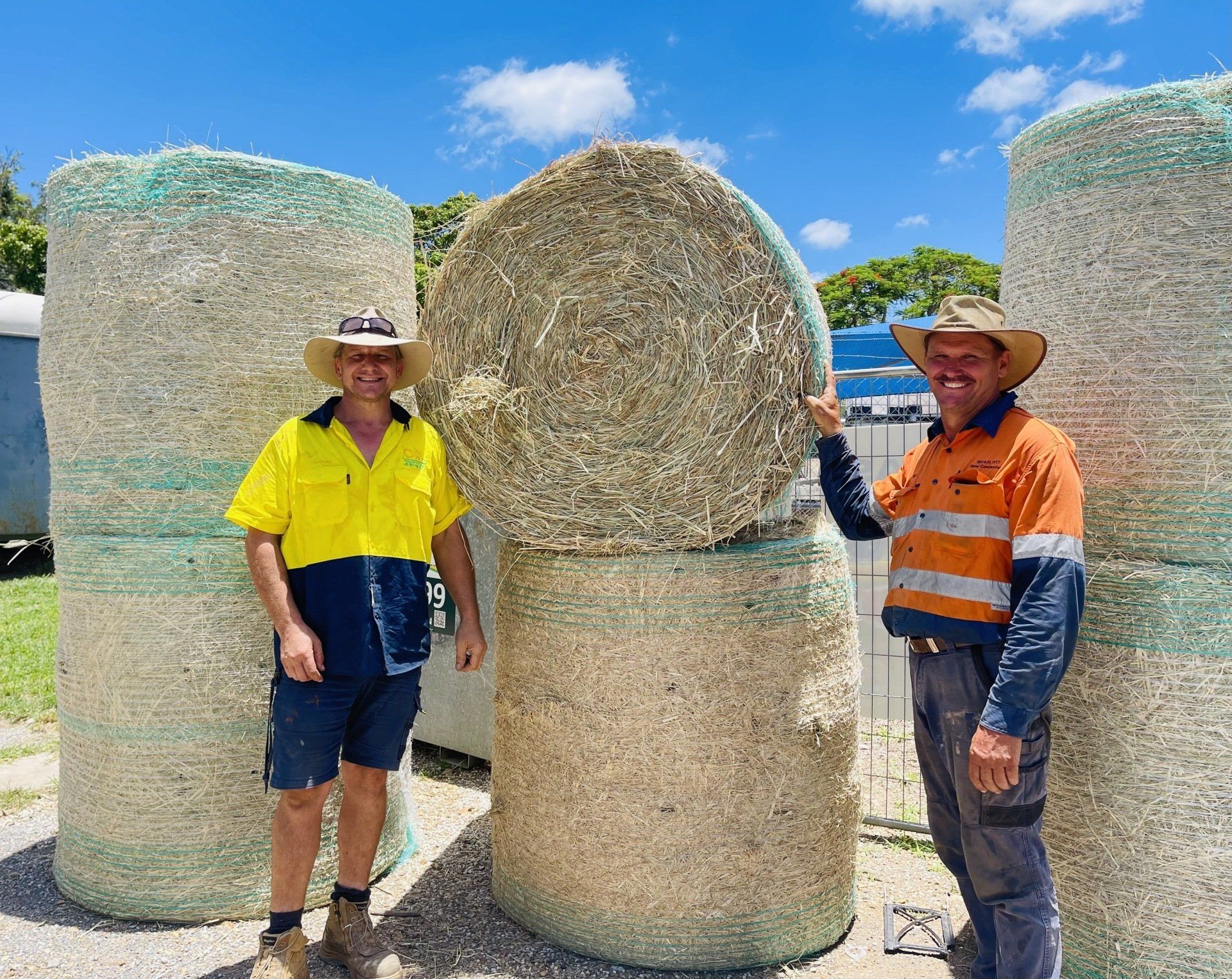 Two men are standing next to a pile of hay bales.