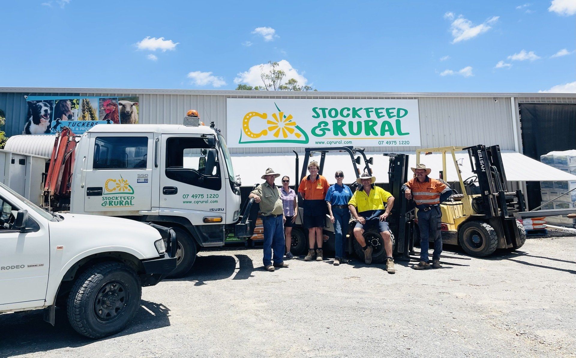 A group of people are posing for a picture in front of a building that says stock feed & rural