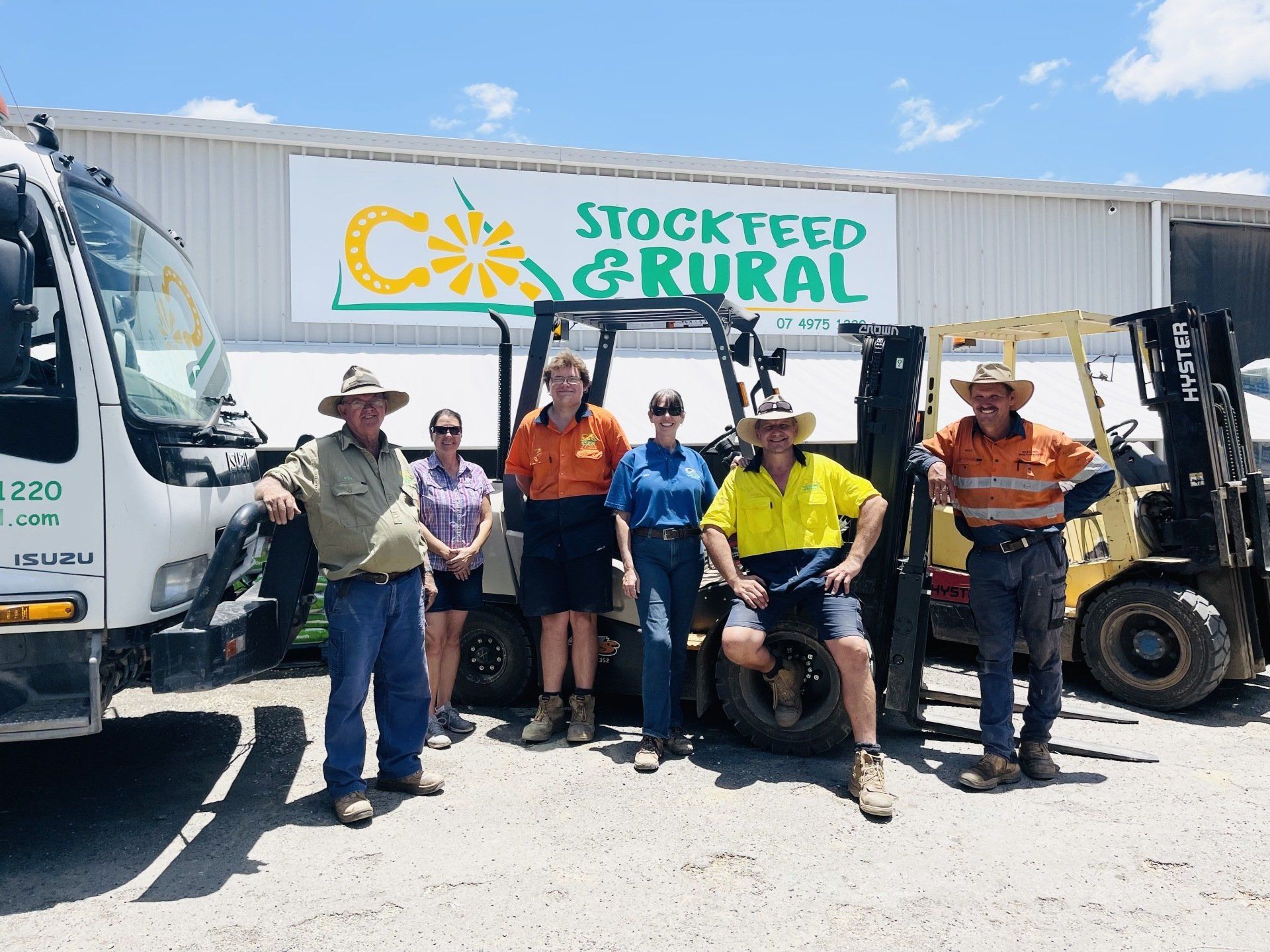 A group of people are posing for a picture in front of a building that says stockfeed & rural.