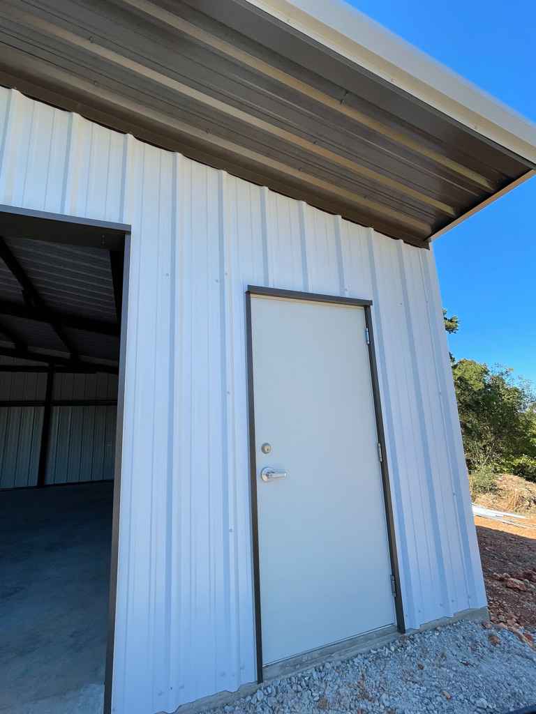 White metal building with a door. Brown trim, concrete floor and gravel base.