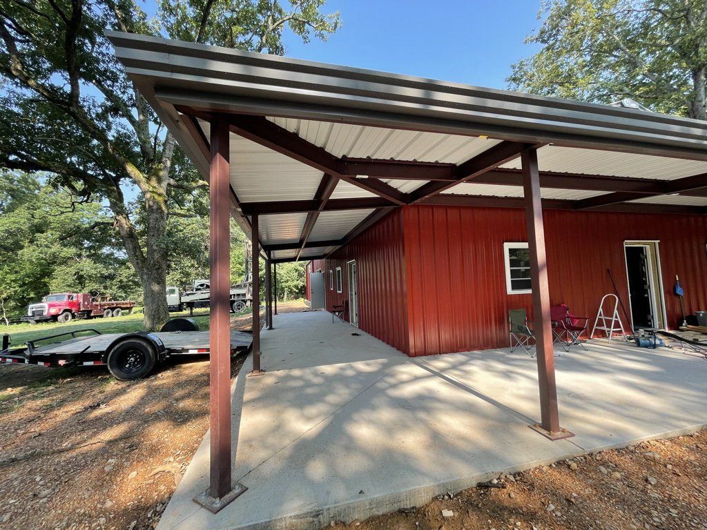 Red building with a brown metal awning and concrete porch. A trailer and trees are in the background.