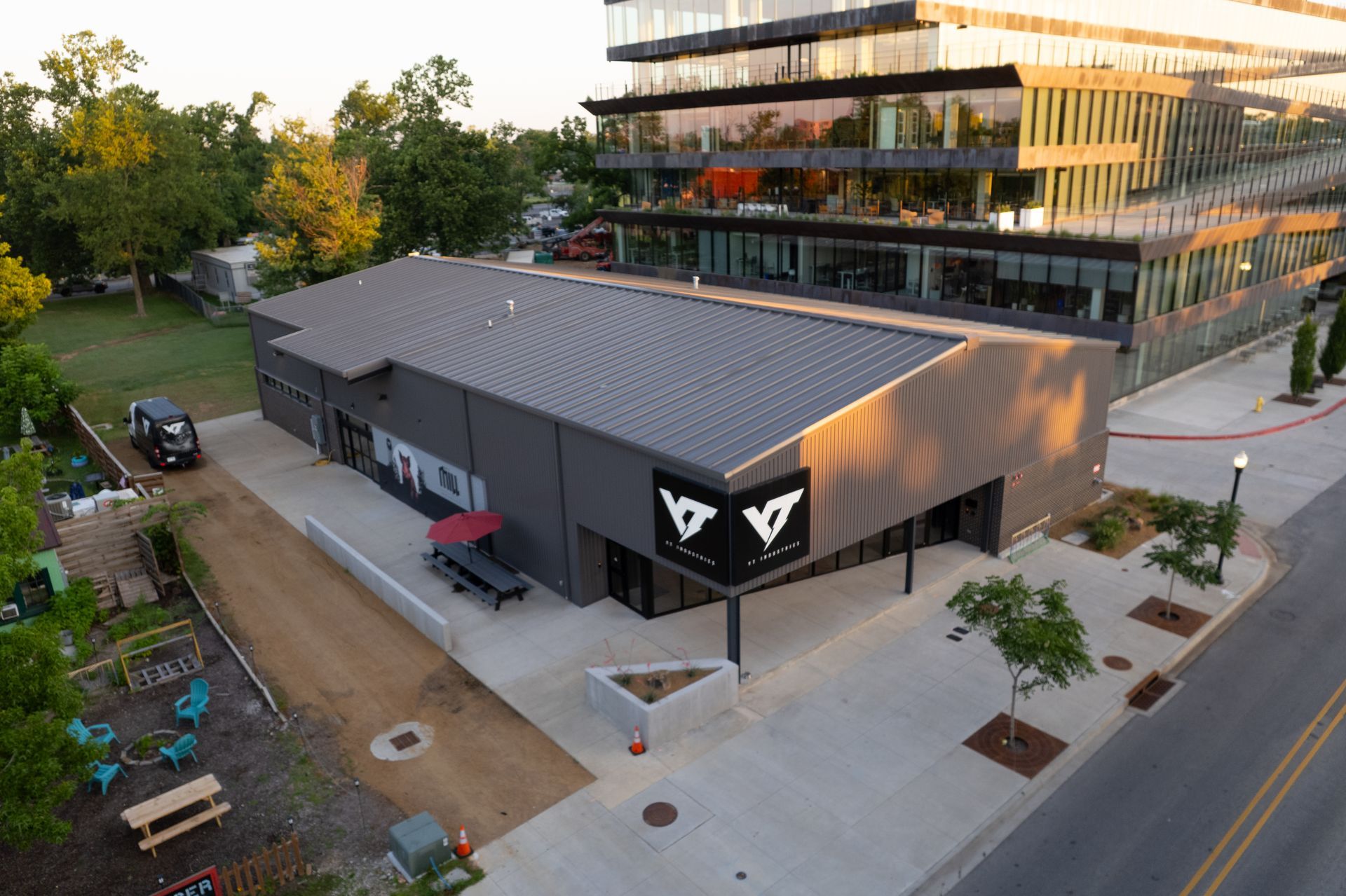 An aerial view of a modern gray building with a black logo, next to a large glass office building.