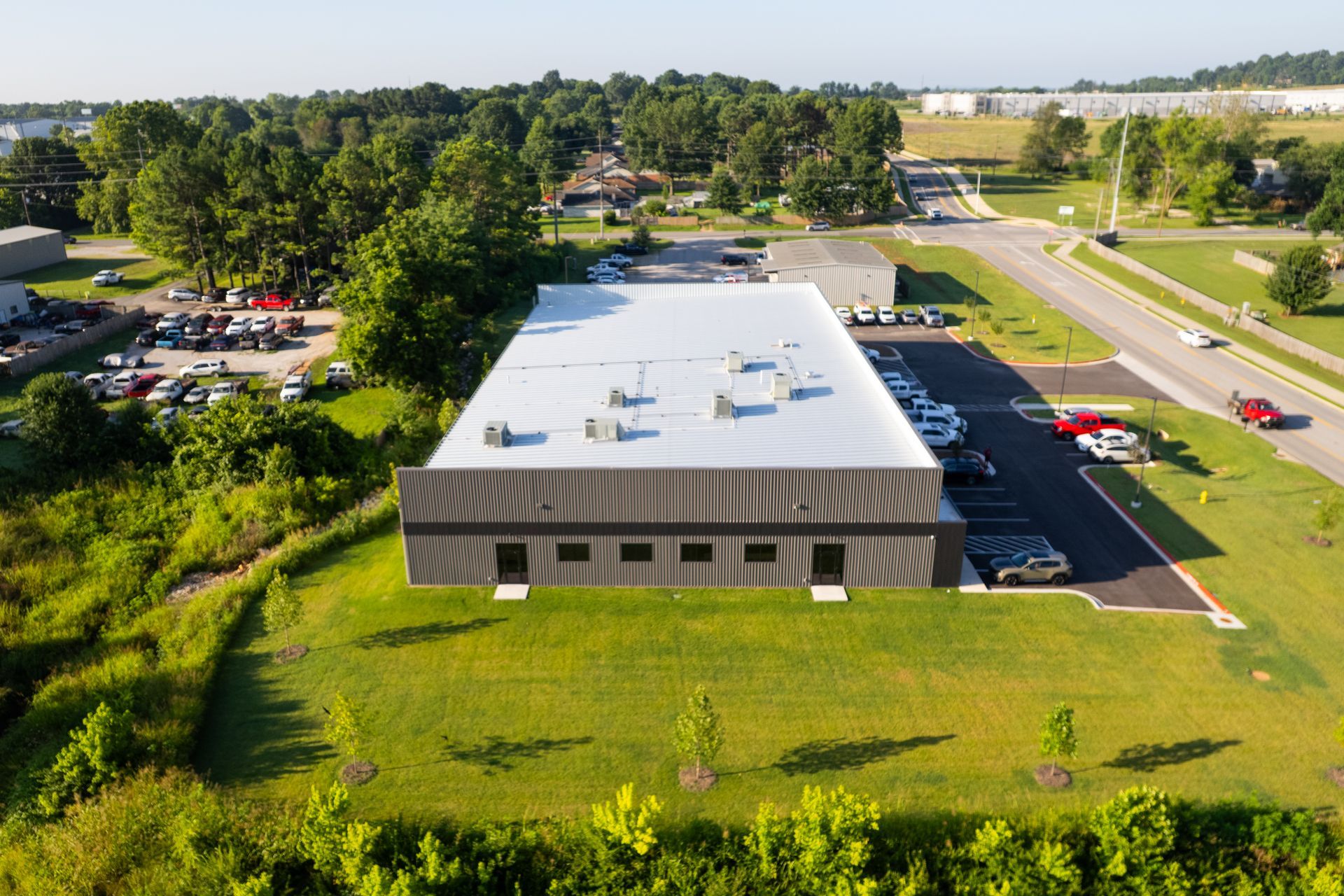 Aerial view of a modern commercial building with a flat roof and dark exterior, surrounded by greenery and parking.