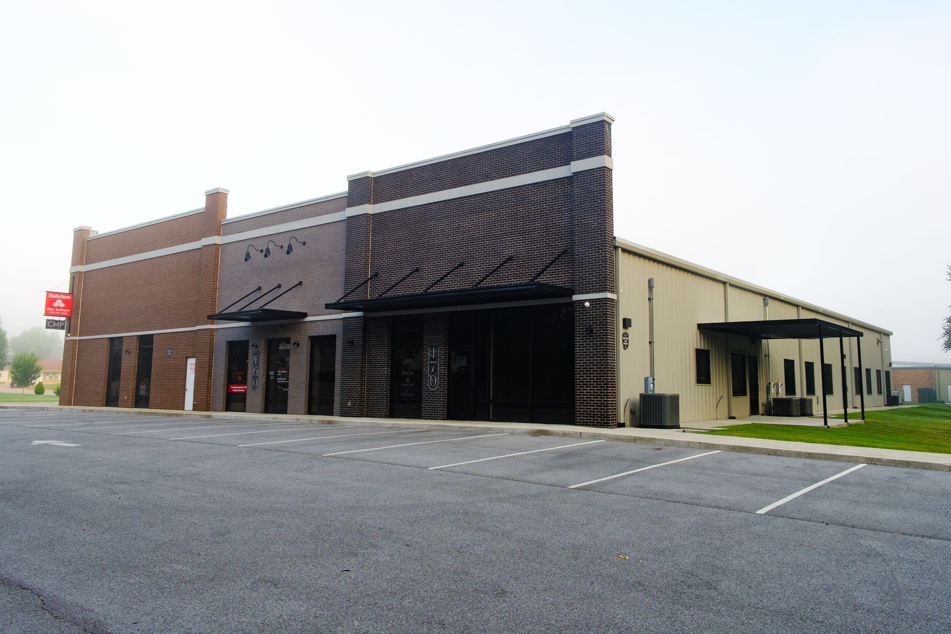 A commercial building with brown brick and a dark facade, with an attached tan metal-sided structure; empty parking lot.