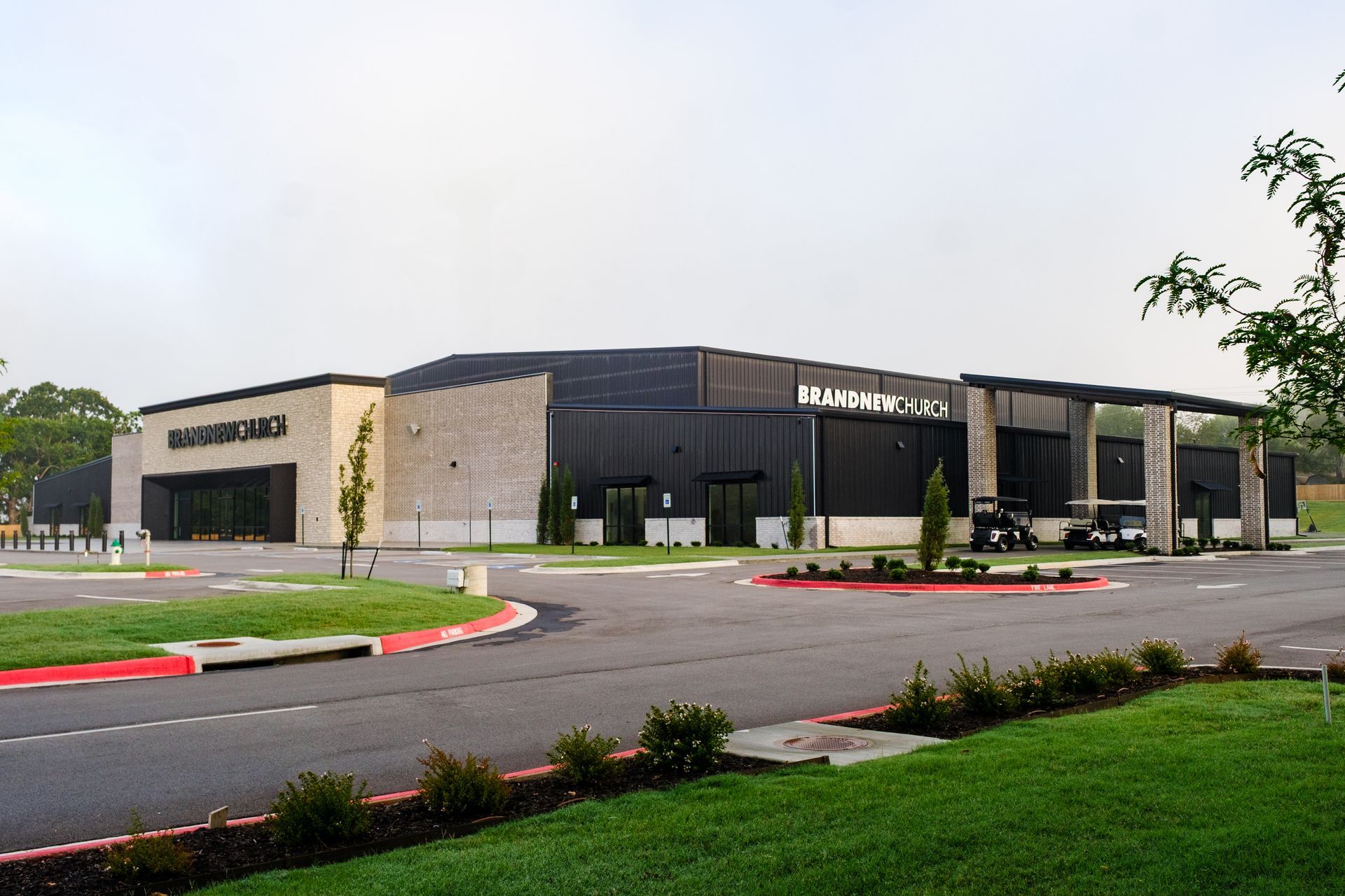 Modern brick and black metal building with circular driveway and green landscaping, 