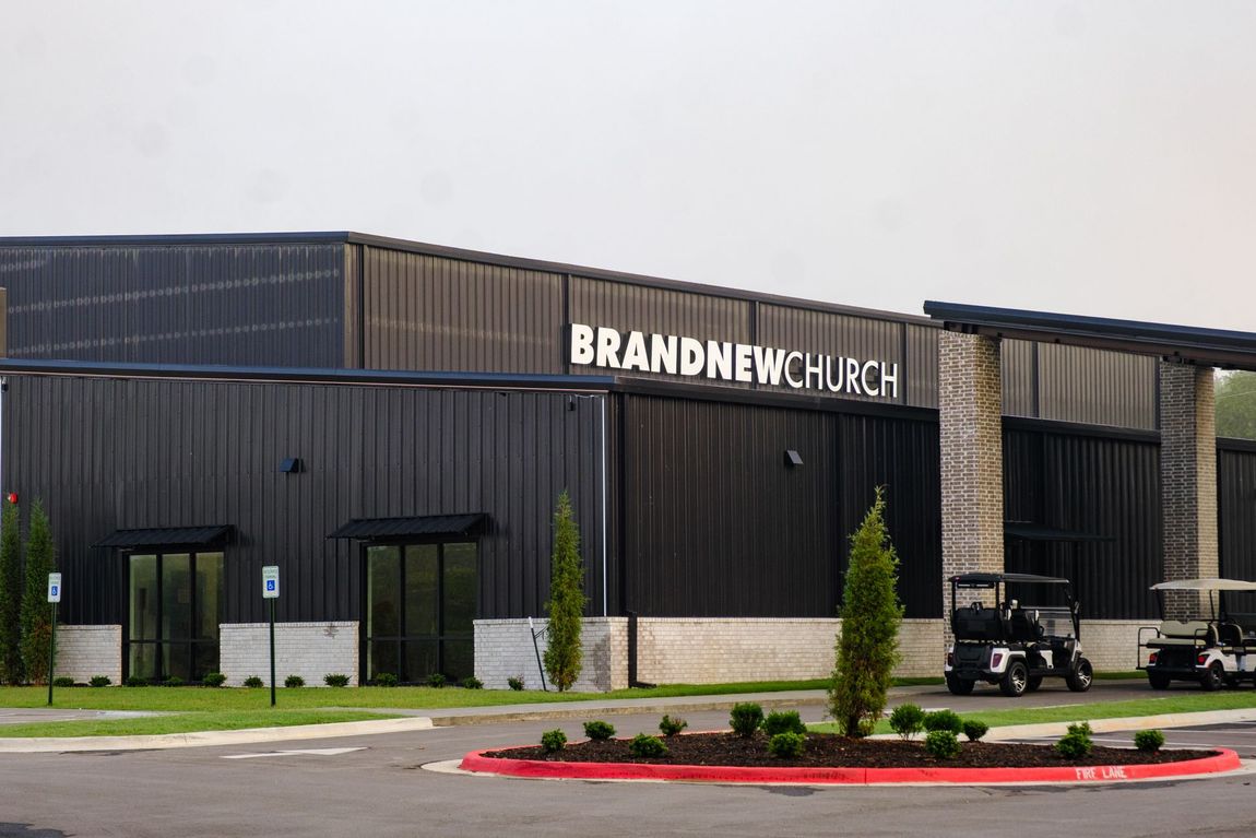 Exterior of Brand New Church, a modern building with a black facade and white text, featuring a driveway and golf carts.
