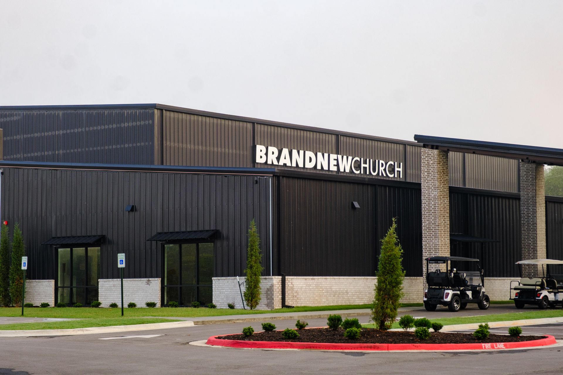 Brand New Church building with dark siding, a stone facade, and golf carts parked outside.