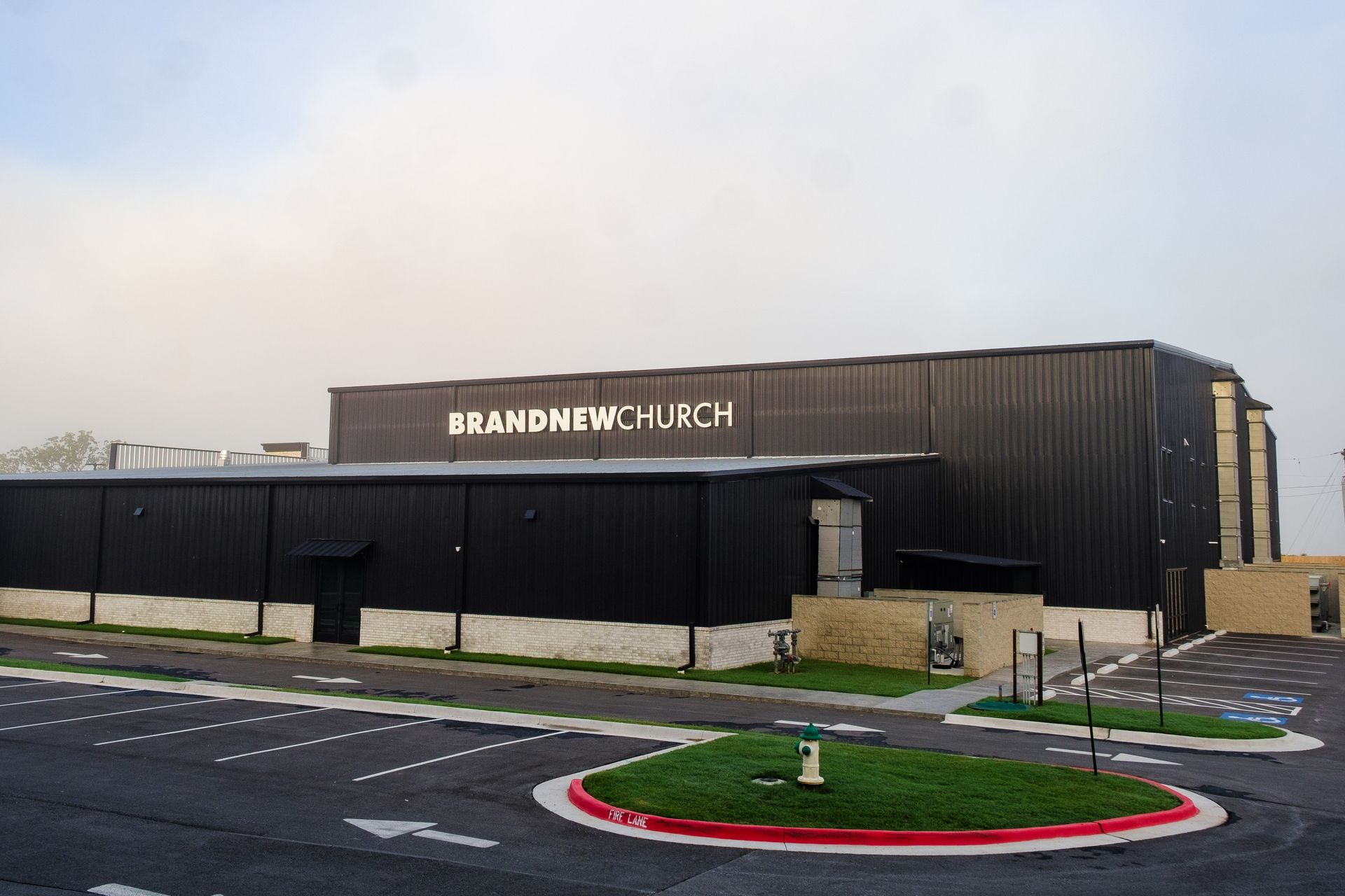 BrandNew Church, a modern black building with a small parking lot on a cloudy day.