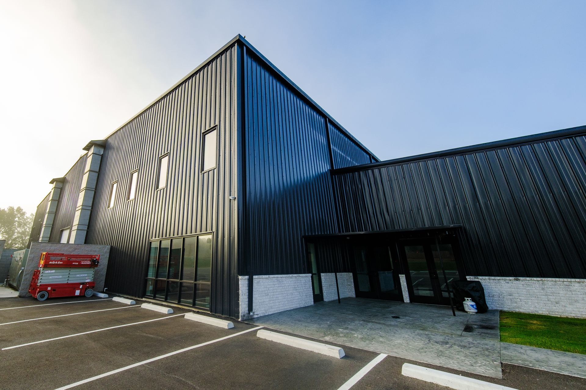 Modern black building with corrugated metal siding, entrance under a dark overhang, and a small parked vehicle visible.