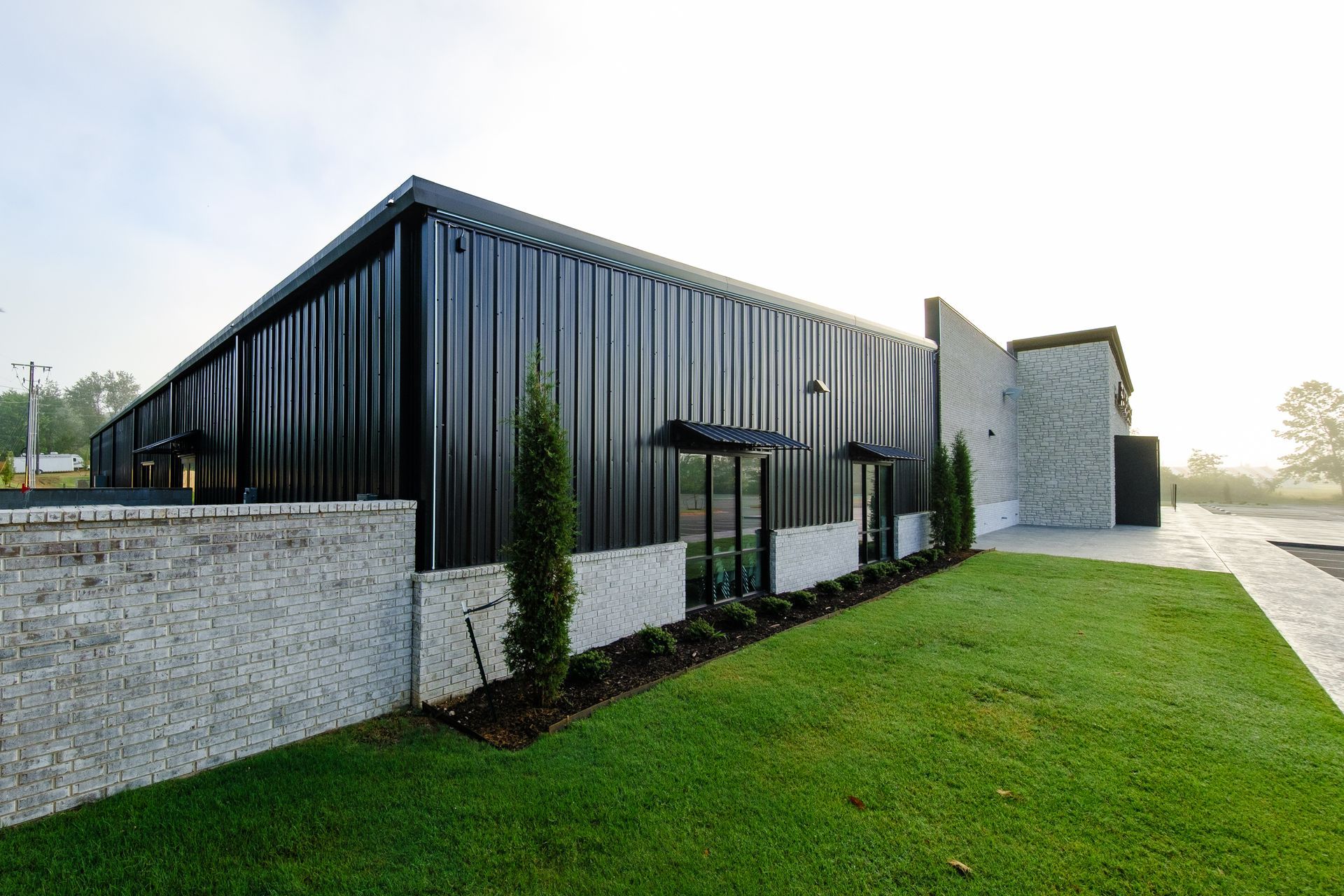 A modern building with black corrugated metal siding and a stone facade, featuring a green lawn and landscaping.