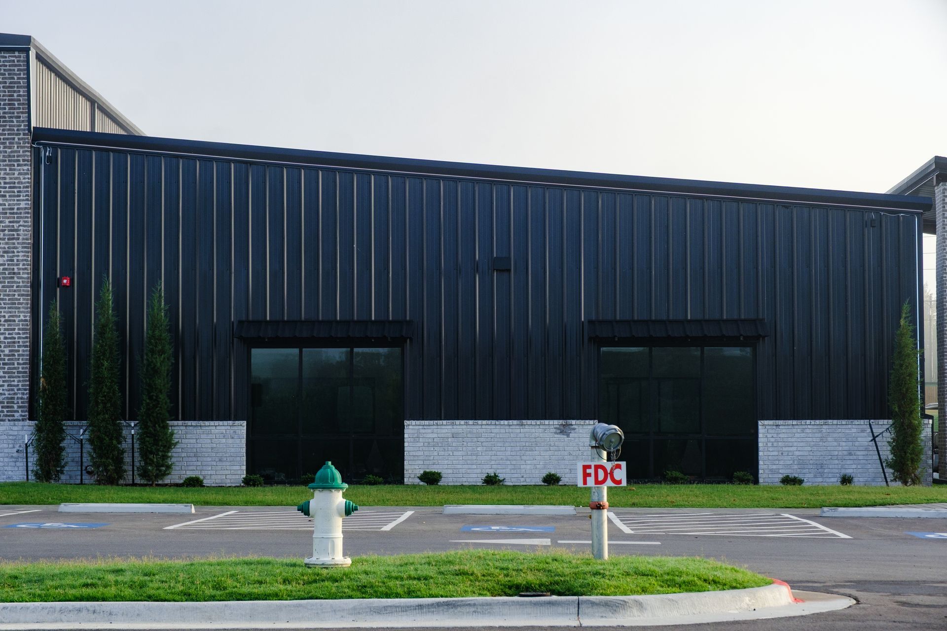 A dark metal building with two large windows, a fire hydrant, and a parking lot.