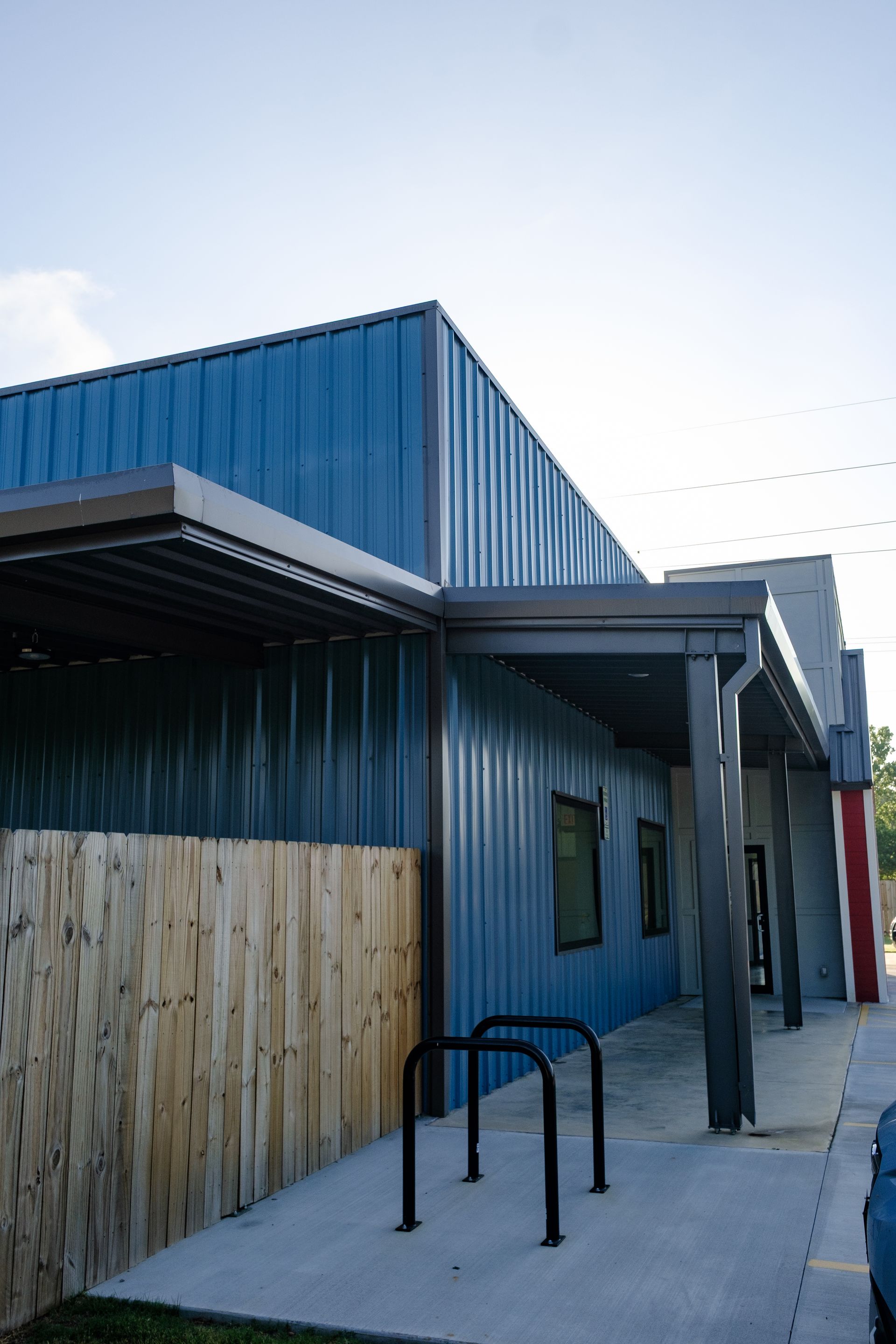 Blue metal-sided building with a covered walkway. A wooden fence and bike rack are in front.