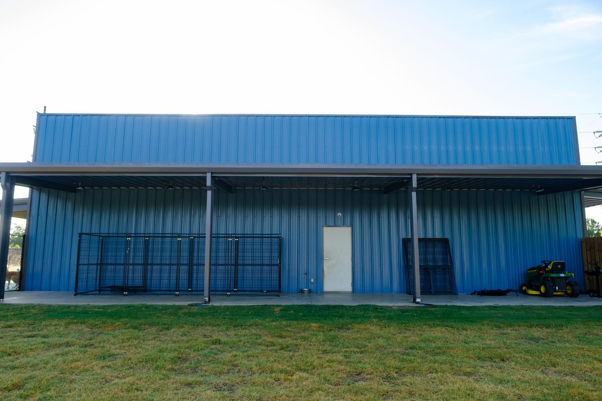 Blue metal building with a covered porch, white door, and green lawn.