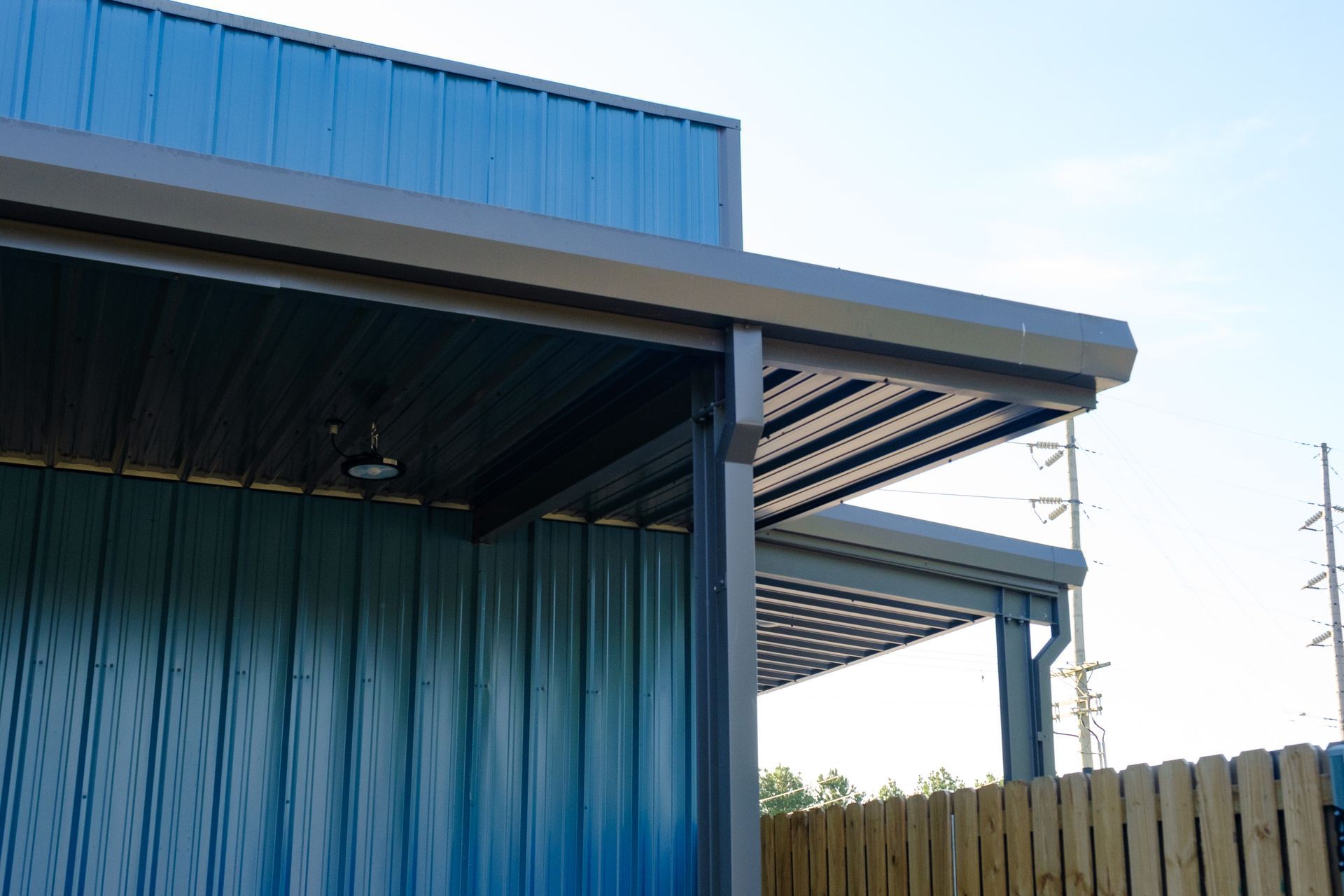 Blue and gray building with a corrugated metal exterior and a pergola roof section; sunny outdoor setting.