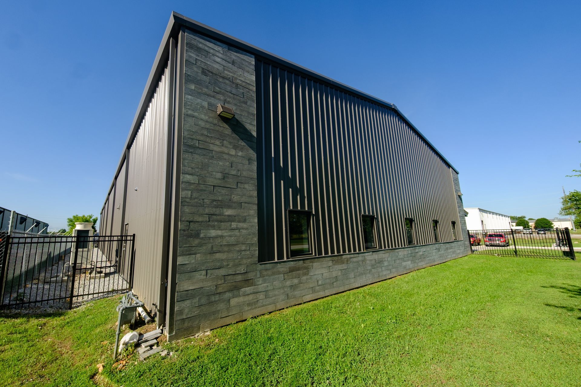 Dark-colored corrugated metal building with a rippled reflective pattern on the side, set on a grassy lawn under a blue sky.