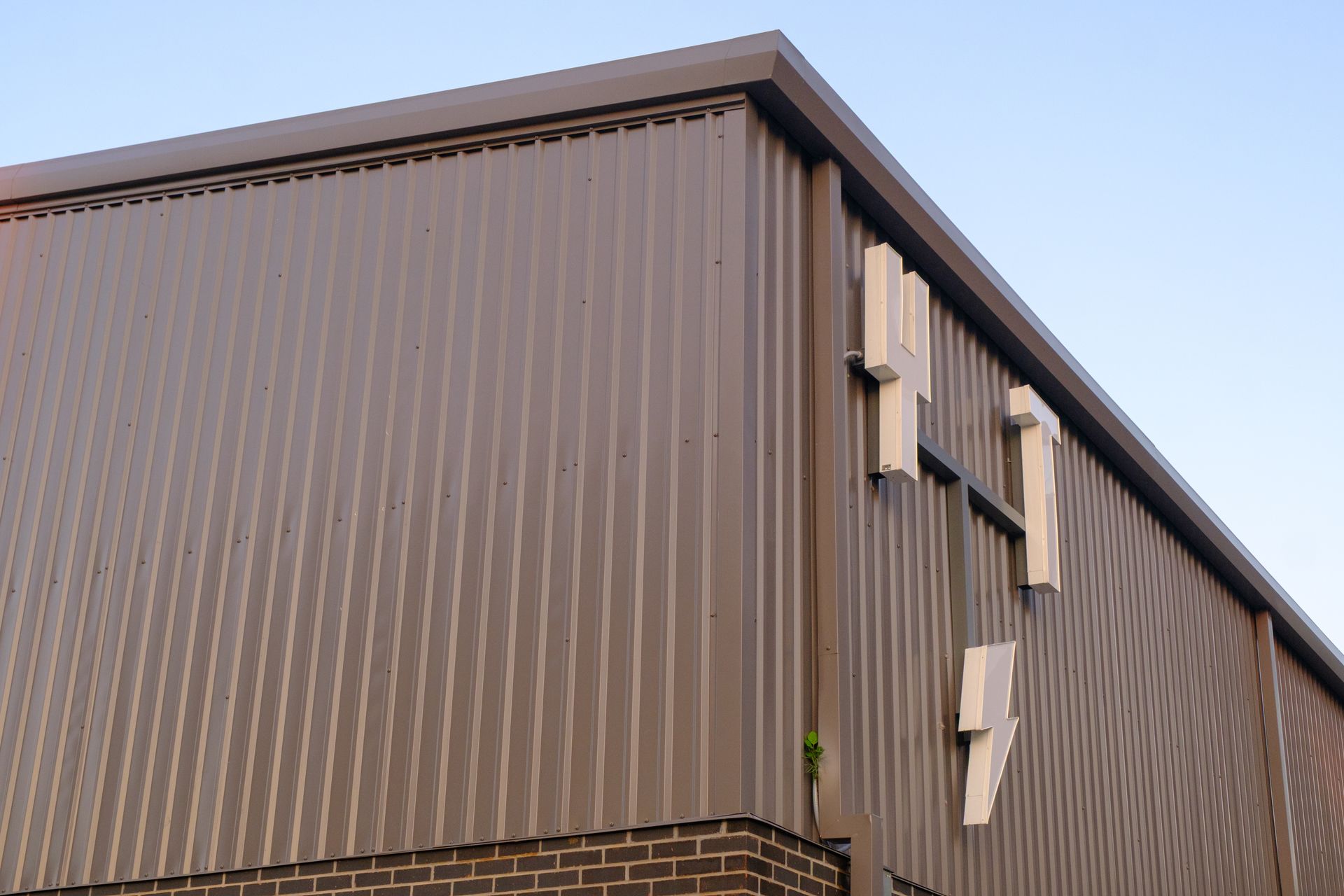 Brown corrugated metal building corner with square windows and white rectangular details, set against a clear blue sky.