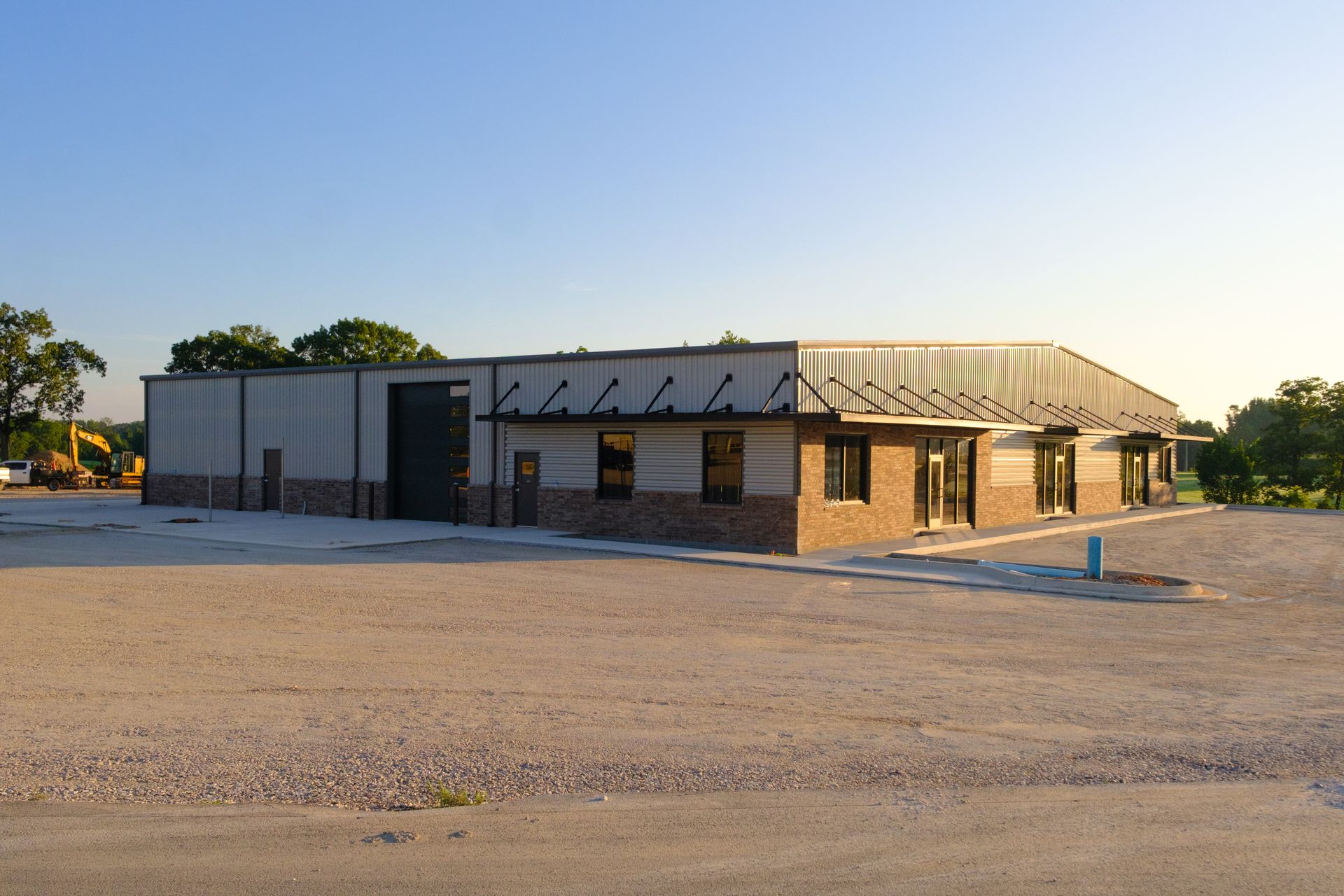 Building with a metal roof and brick base; gravel lot in front.