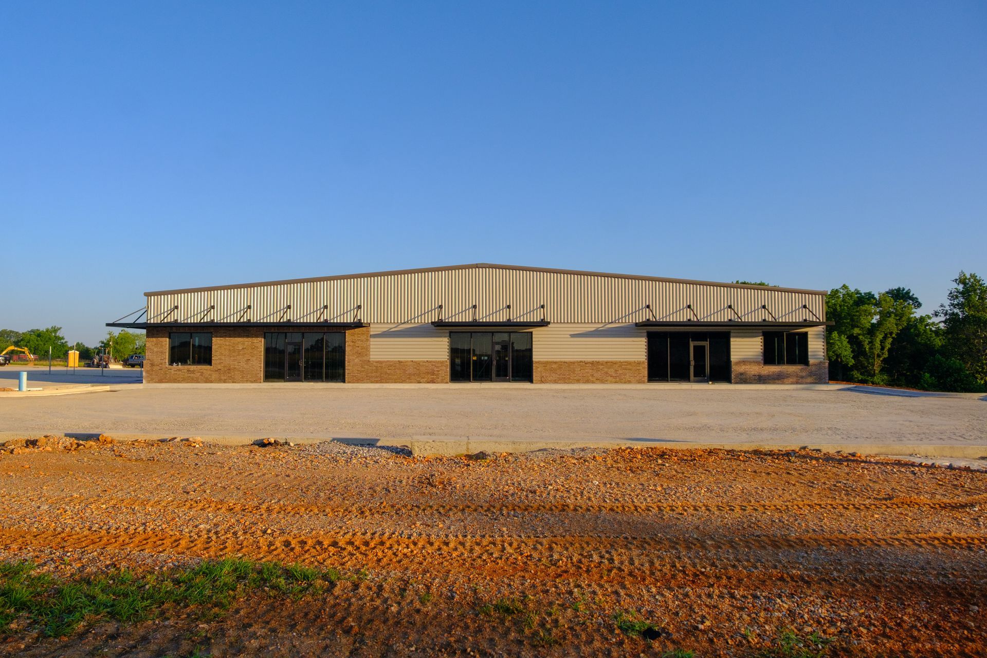 A single-story commercial building with a brown facade, corrugated metal roof, and large windows under a clear blue sky.