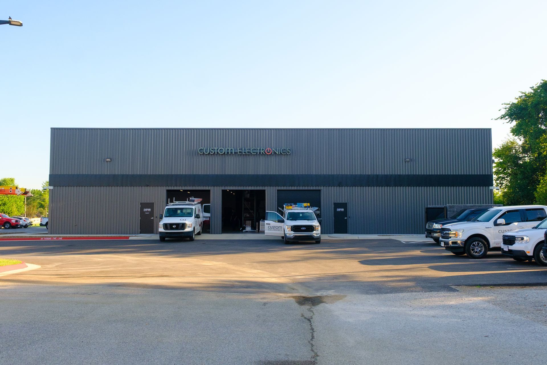 Exterior of a business with a gray facade, open garage bays, and service vehicles parked in front. 