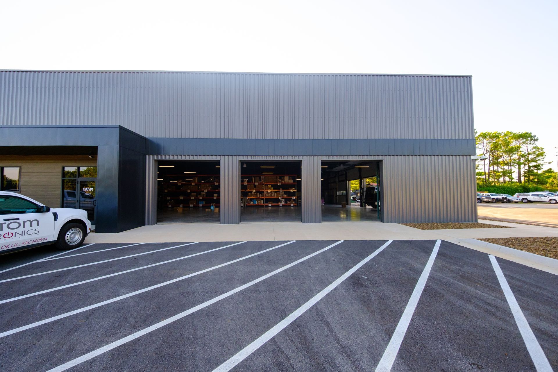 Exterior of a gray metal building with three open garage doors, revealing workout equipment inside. A white truck is parked to the left.