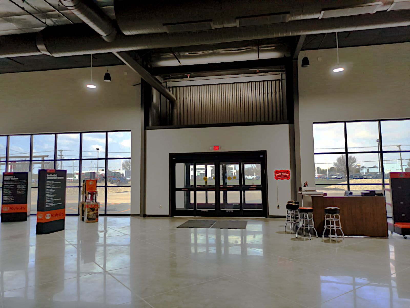An empty, modern lobby with glass doors, tall windows, and a stage area. The floors are reflective, and there are information displays.