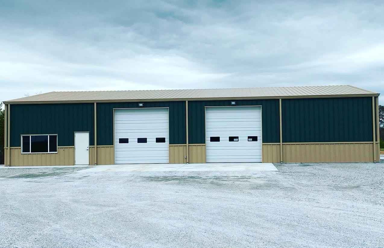 Dark green and beige metal building with two garage doors, a small window, and a white door. Cloudy sky overhead.