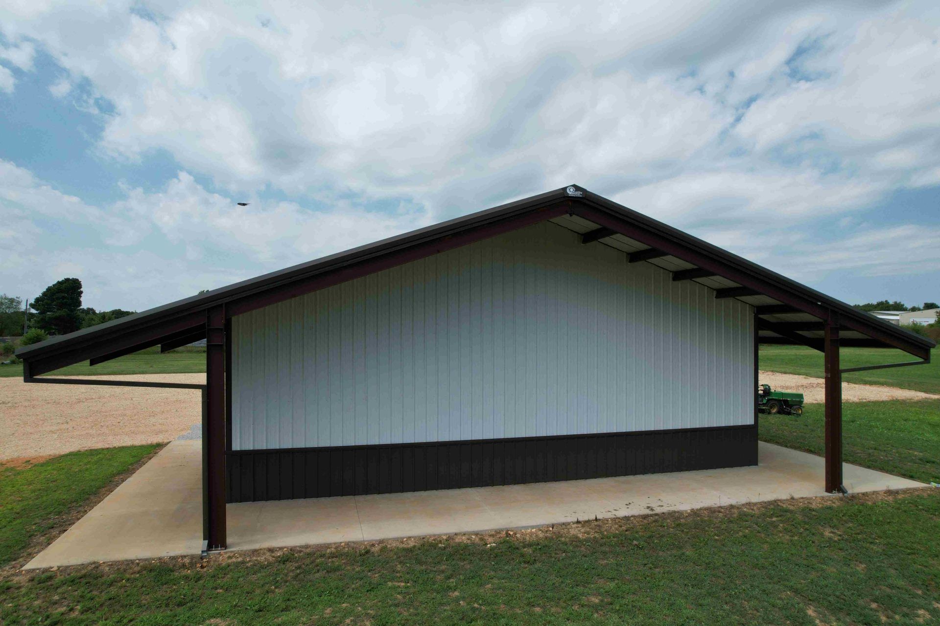 A metal-sided shelter with a brown roof and support beams, white upper walls and brown lower walls, on a concrete slab, outdoors.
