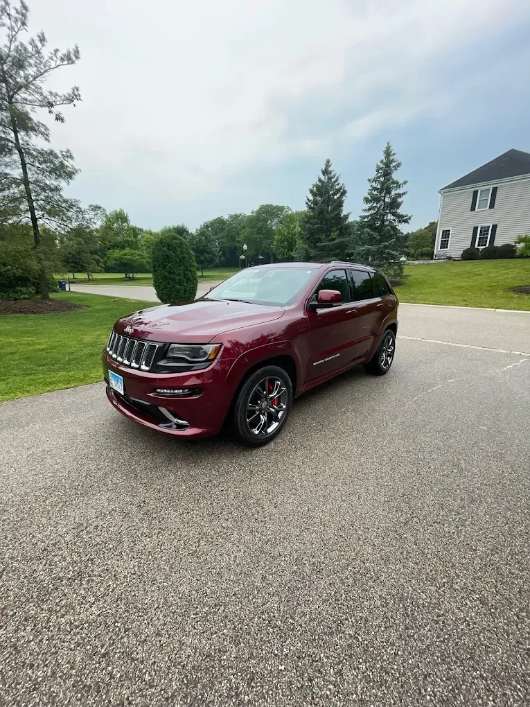 Maroon SUV parked on a suburban driveway beside a lawn and house under cloudy skies