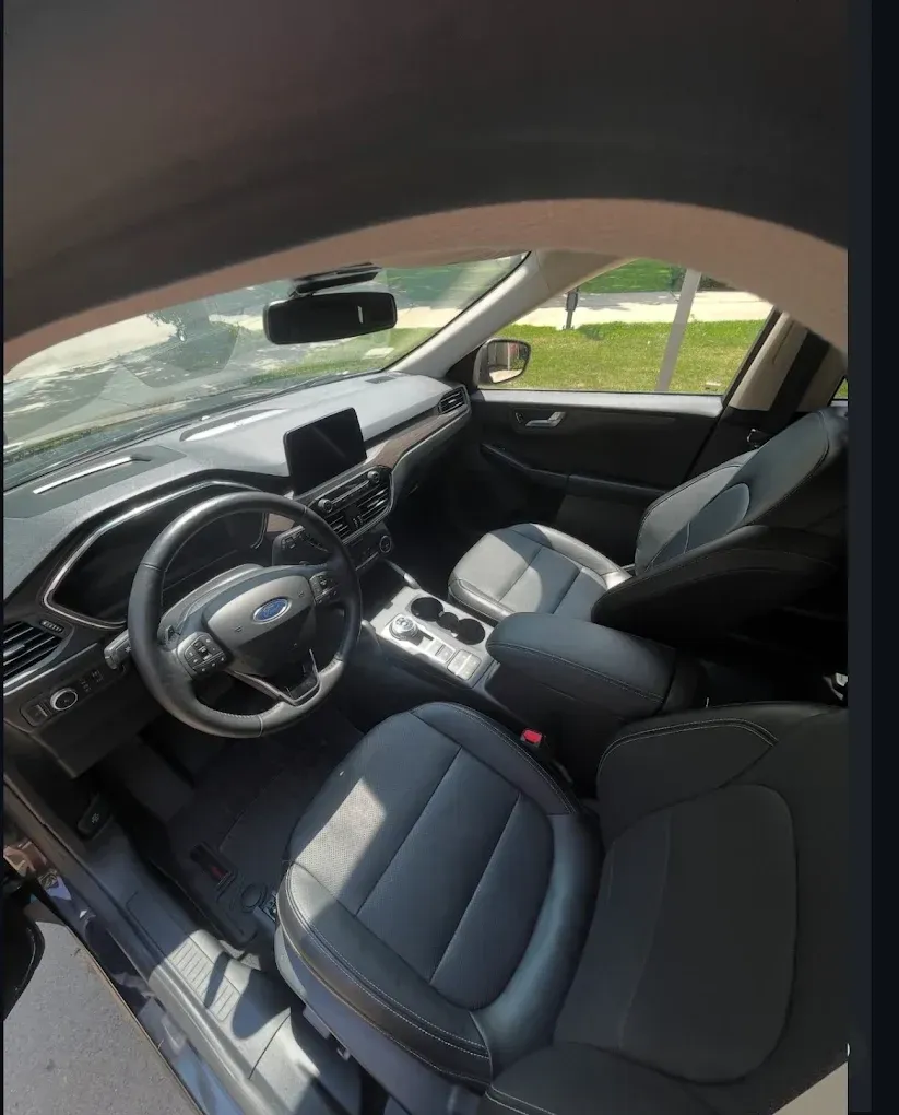 Car interior with black leather seats, steering wheel, dashboard screen, and center console seen from the open door