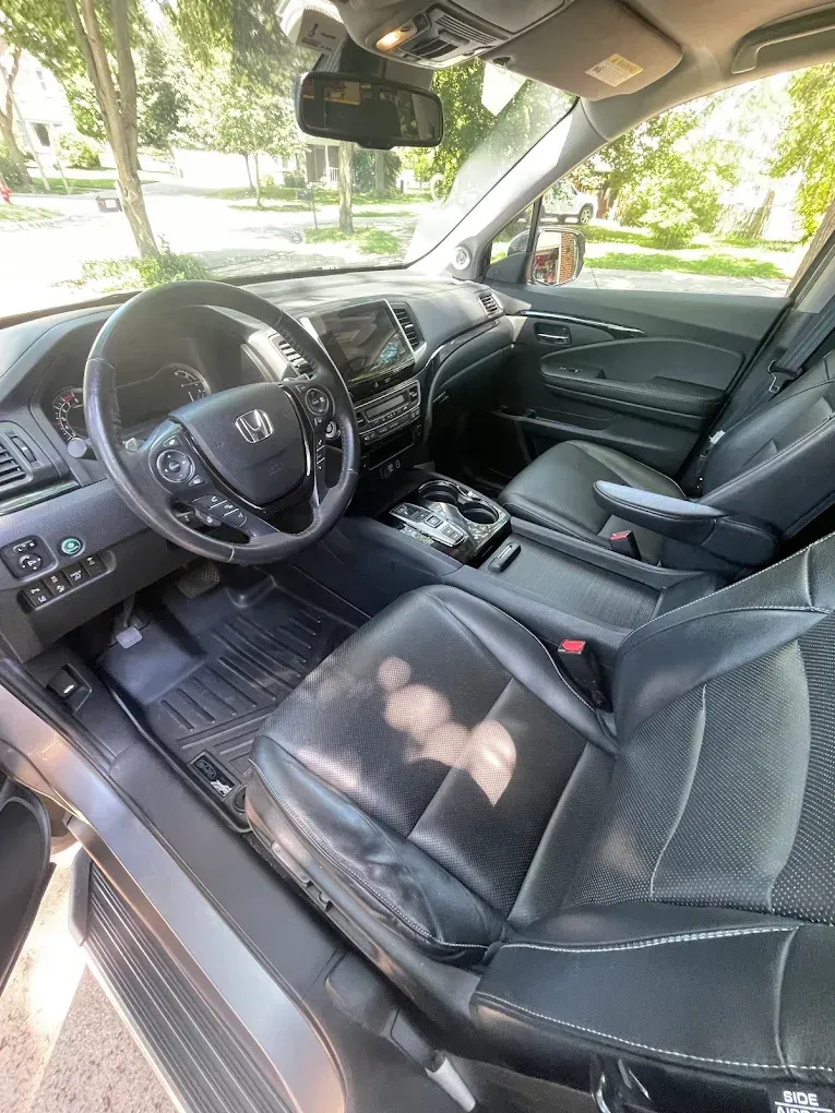 Car interior with black leather seats, steering wheel, and center console, parked in daylight