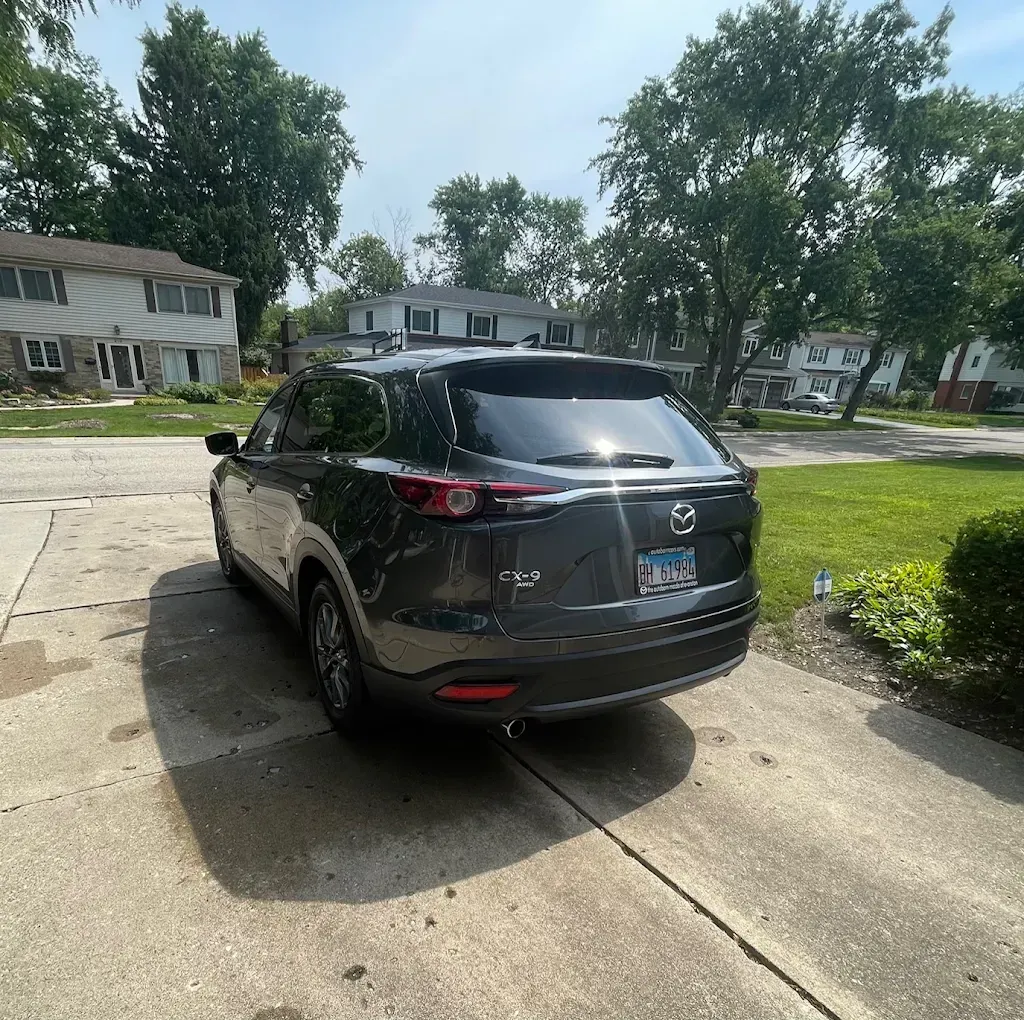 Black Mazda SUV parked in a driveway on a sunny suburban street with houses and trees nearby
