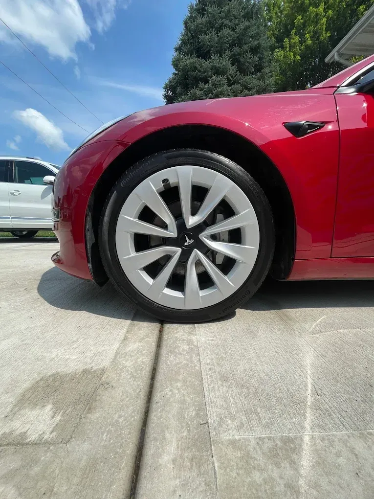 Red car parked on a driveway, close-up of the front wheel and fender.