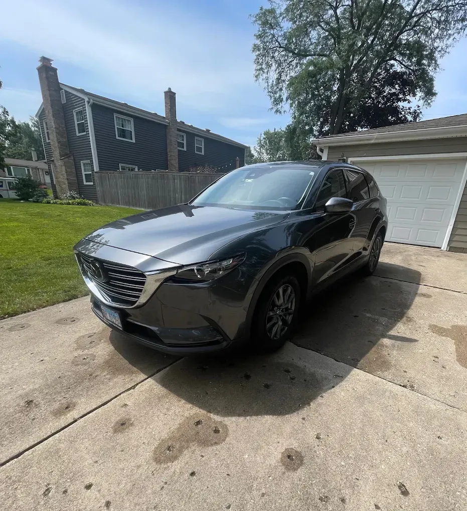 Gray SUV parked in a driveway beside a garage on a sunny day.
