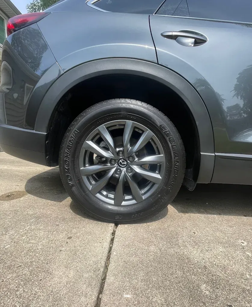 Close-up of a gray SUV’s rear wheel and side panel parked on a concrete driveway.