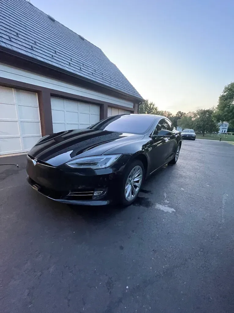 Black sports car parked in a driveway beside a house at dusk