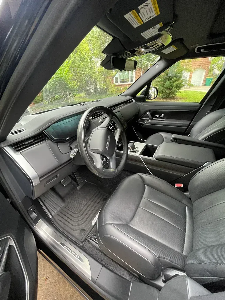 Luxury car interior with black leather seats, steering wheel, and sunroof, viewed from the open driver’s door