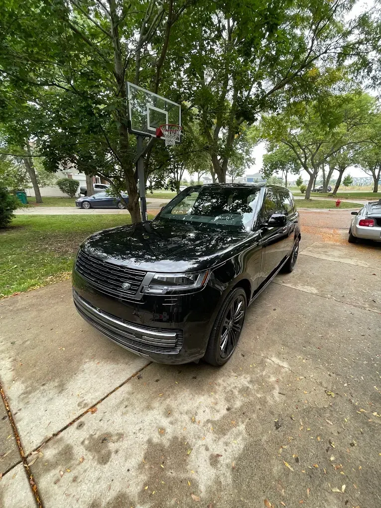 Black SUV parked on a driveway under trees, with a basketball hoop overhead