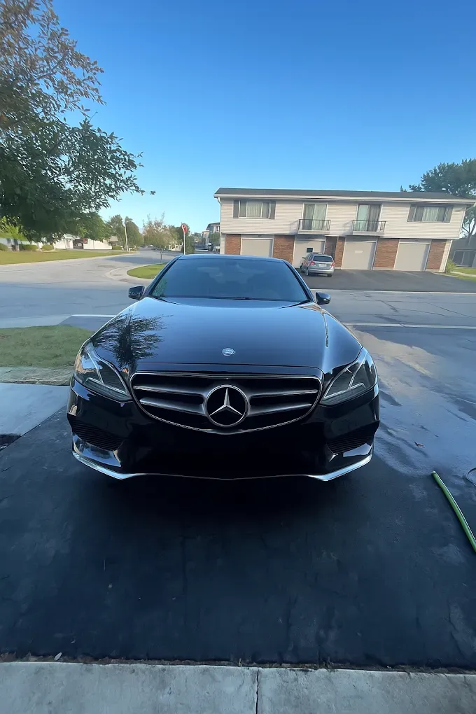 Black Mercedes sedan parked on a driveway in front of a house under a clear blue sky