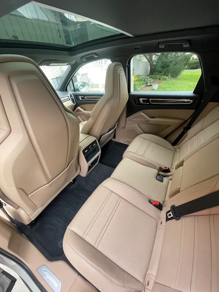 Back seat of a beige luxury SUV with leather seats and panoramic sunroof, viewed from the open door
