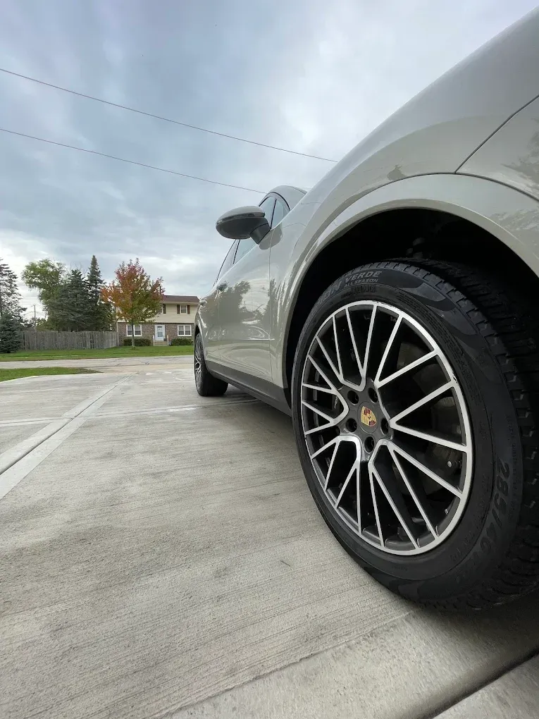 Low-angle view of a silver car’s rear wheel and side panel on a concrete driveway