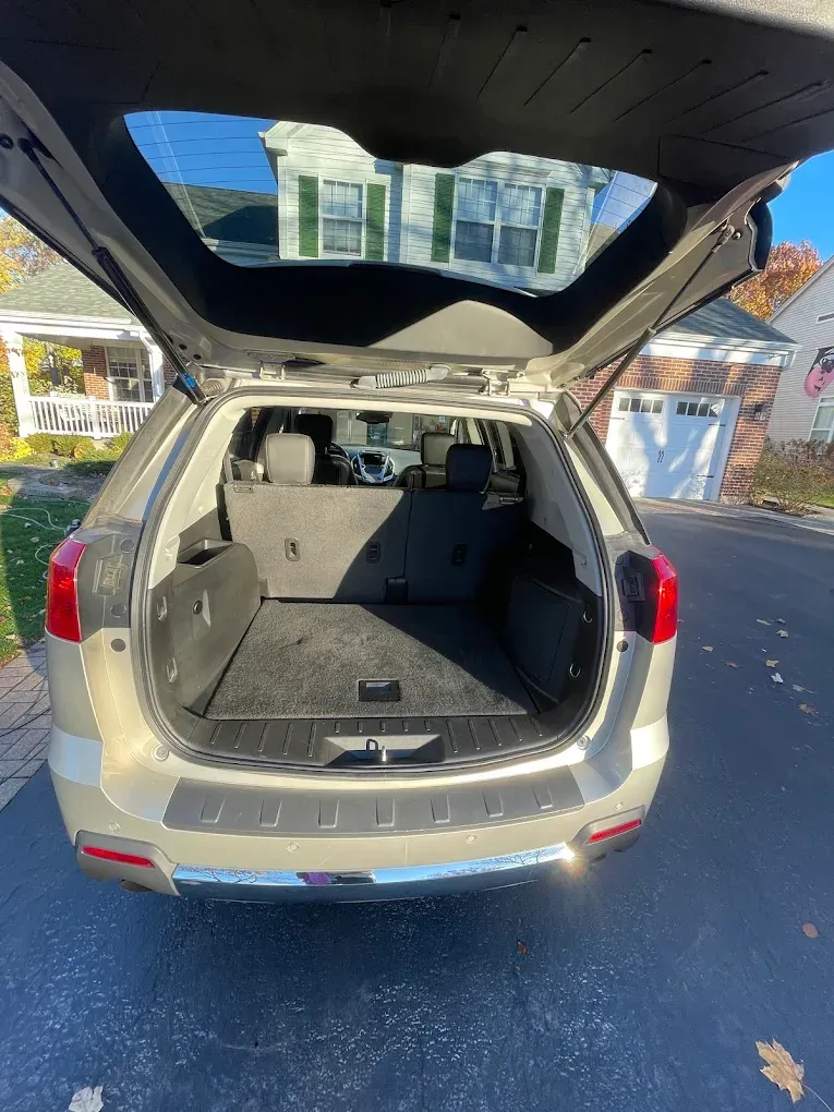 Open SUV cargo area with rear hatch raised, showing empty trunk space in a driveway.