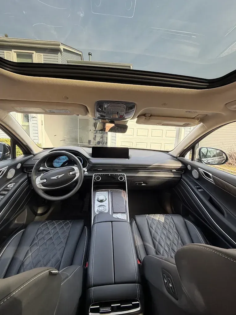 Luxury car interior with black quilted seats, panoramic sunroof, and dashboard view from the back seat